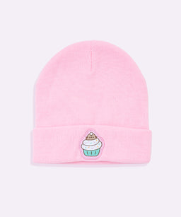 A pink knit beanie with a folded cuff. It features a small cupcake embroidery patch on the cuff, adding a cute, whimsical detail. The pastel color and soft knit suggest a unisex or kids-friendly style, with a cozy, casual look suitable for everyday wear.