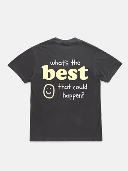 A dark crew-neck short-sleeve T-shirt featuring a playful back graphic that reads “what’s the best that could happen?” in pale yellow/cream letters with a smiley face. The design is graphic-driven and casual, suitable for a unisex audience based on cut and styling. Visible materials suggest a soft cotton tee, in a charcoal color with light-colored print for high contrast.