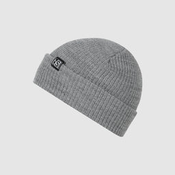 A gray knitted beanie with a folded cuff and a small black label on the cuff. Appears designed as a unisex, gender-neutral accessory; the visible fabric is a ribbed knit in heather gray, with a simple, minimalist style.
