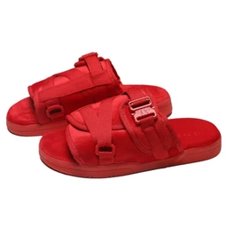 These are crimson red open-toe slide sandals with multiple fabric straps and an adjustable buckle fastening. The chunky, cushioned sole and sporty strap design suggest a casual, everyday wear style for a unisex audience, with a bright red color and matte fabric straps as the standout details. Notable materials appear to be fabric straps and a rubber-like sole in matching red.