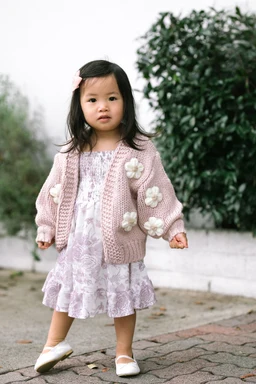 Pink knit cardigan with cream flower appliqués on young child, front view.