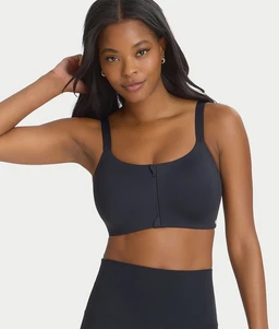 A woman wearing a dark gray front-closure sports bra with wide straps, standing against a light background.