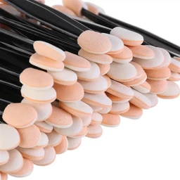 A close-up of many disposable dual-ended sponge applicators with black plastic handles and peach and white oval sponge tips, fanned out against a white background.