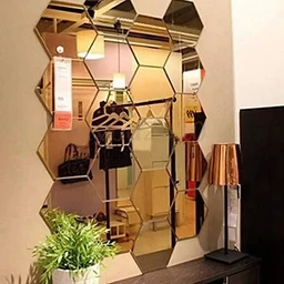 Hexagonal silver mirror tiles arranged on a pale wall beside a lamp, a potted plant, and a shelf of handbags reflected in the mirrors.