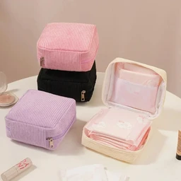 Four square corduroy zip pouches in pink, black, lilac and cream sit on a white table, with the cream one open to show pink sanitary pads inside.