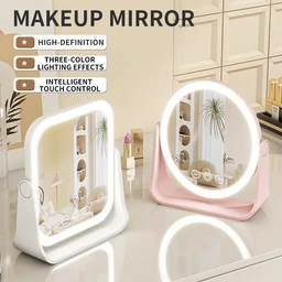 Two illuminated makeup mirrors with white and pink frames sit on a cream and white vanity surface in a bright, minimal room with shelves holding cosmetics and small plants.