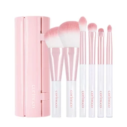 Six pink-and-white makeup brushes with synthetic bristles stand beside a pink cylindrical roll case on a plain white background.