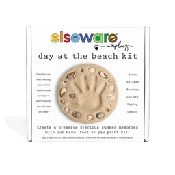 A boxed Day at the Beach kit showing a tan sand-cast disc with a handprint decorated with shells and pebbles, set against a white background.