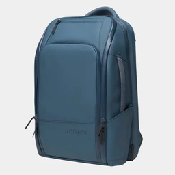 A slate blue Nomatic backpack shown from a three-quarter angle against a light gray background.