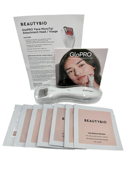 A white handheld GloPro microneedling roller tool with a stainless steel roller head lies beside an instruction card, a GloPro box, and several pink foil-wrapped Residue Eraser and skin prep pads on a white background.