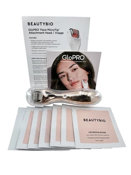 A gold-handled microneedle face roller with a stainless steel head, shown beside a printed instruction sheet, a GloPro brochure featuring a smiling woman, and a stack of white residue eraser and skin prep sachets on a white background.