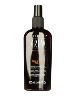 A tall dark brown spray bottle with a black pump nozzle and white and orange American Crew label, shown against a plain white background.