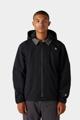 A person faces forward against a light gray background, wearing the 686 x Malbon Mens Caddie Performance Jacket by 686—a black hooded jacket with a front zipper and a small circular logo on the left chest.
