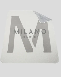 Cream throw blanket with a large gray Milano logo on the top side, partially folded to reveal a gray plush underside.