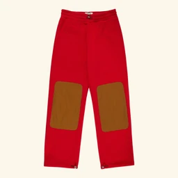 These are bright red pull-on pants with contrasting brown knee patches. The design features an elastic waistband and tapered cuffs, with large brown knee panels for a rugged, outdoor look. The styling and size suggest they’re intended for children, suitable for a unisex sporty/off-road vibe. Visible material appears to be soft knit fabric with reinforced knee patches.